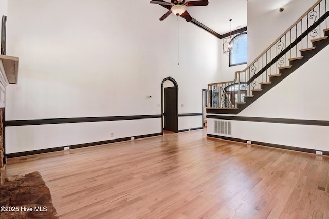 unfurnished living room featuring visible vents, wood finished floors, stairway, baseboards, and a high ceiling