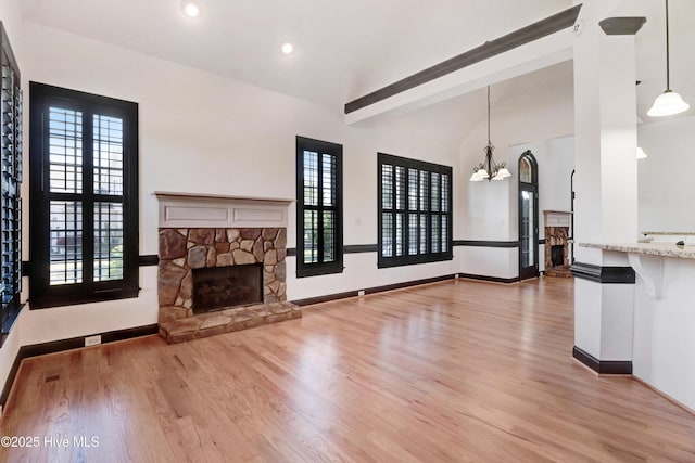 unfurnished living room with a fireplace, vaulted ceiling, baseboards, light wood finished floors, and an inviting chandelier