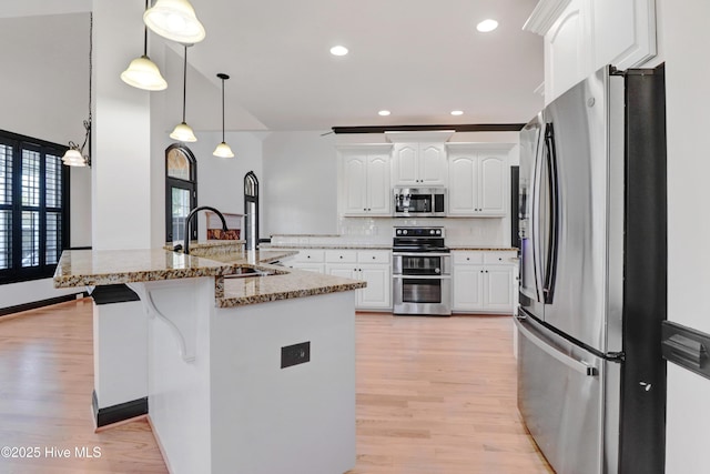 kitchen with appliances with stainless steel finishes, a sink, light stone counters, white cabinets, and light wood-style floors