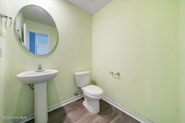 half bathroom featuring toilet, baseboards, a sink, and wood finished floors