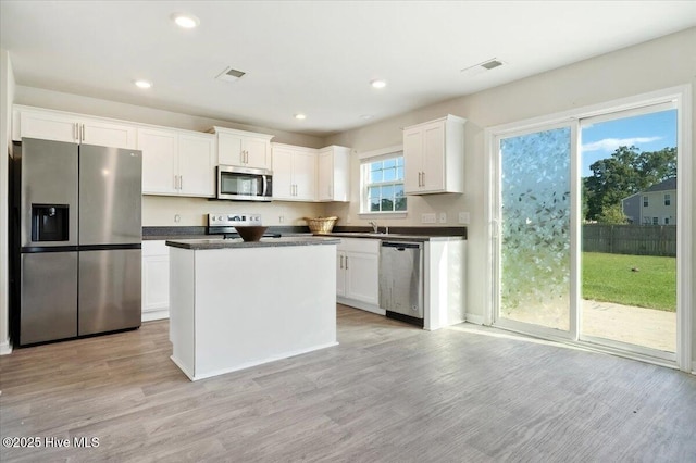 kitchen featuring dark countertops, appliances with stainless steel finishes, white cabinetry, light wood-type flooring, and visible vents