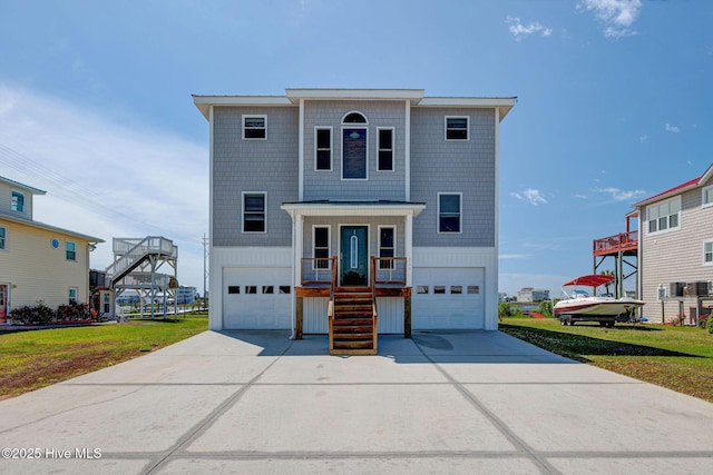 beach home featuring stairs, a garage, concrete driveway, and a front lawn