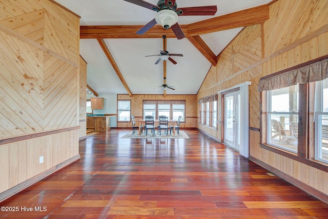 unfurnished dining area with wooden walls, ceiling fan, beam ceiling, high vaulted ceiling, and hardwood / wood-style flooring