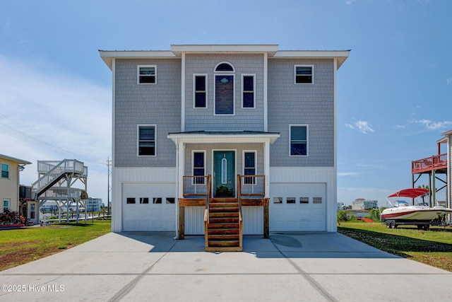 beach home with an attached garage, concrete driveway, and stairs