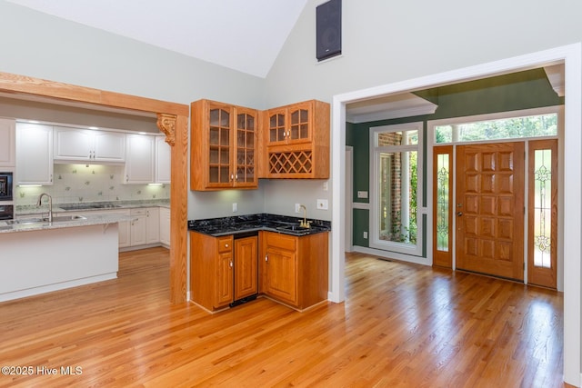 kitchen with light wood-style floors, a sink, high vaulted ceiling, and glass insert cabinets