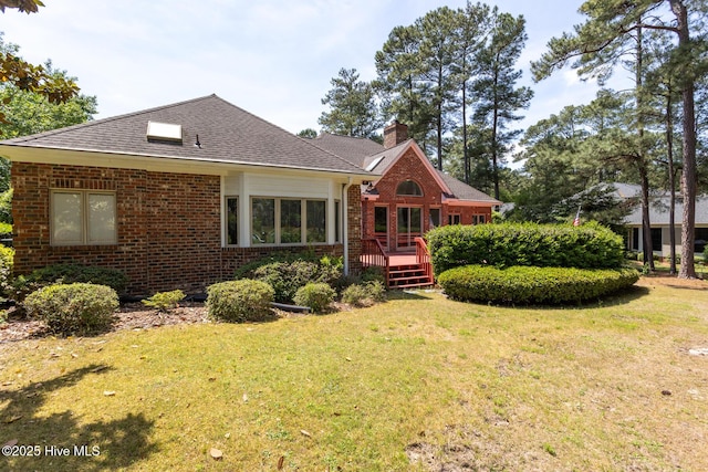 view of front of property with a chimney, roof with shingles, a wooden deck, brick siding, and a front lawn