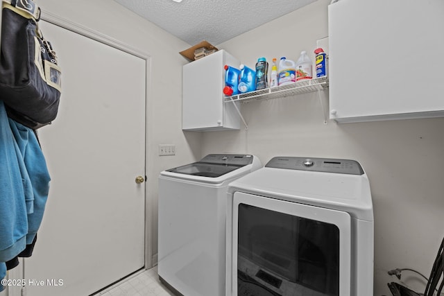 laundry room featuring washing machine and clothes dryer, a textured ceiling, and cabinet space