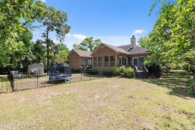rear view of property featuring fence, a trampoline, a lawn, and brick siding