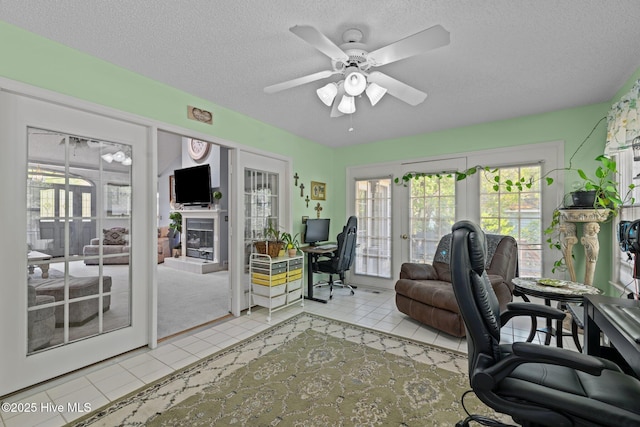 tiled office space featuring a ceiling fan, a textured ceiling, and a glass covered fireplace