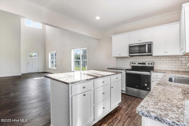 kitchen with appliances with stainless steel finishes, ornamental molding, decorative backsplash, a kitchen island, and dark wood-style floors
