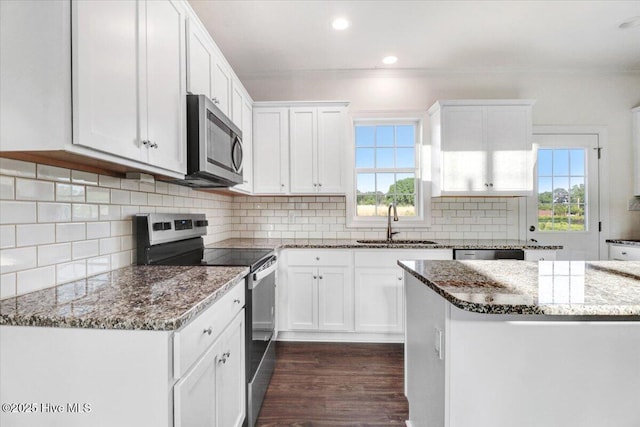 kitchen with dark wood-style floors, dark stone counters, white cabinets, a sink, and stainless steel appliances