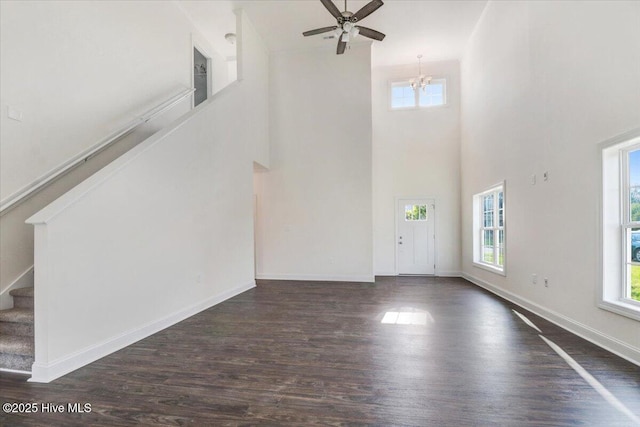 unfurnished living room with dark wood-style flooring, a high ceiling, ceiling fan with notable chandelier, baseboards, and stairway