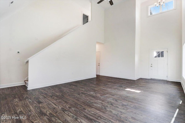 unfurnished living room with baseboards, dark wood-style flooring, a towering ceiling, and stairway