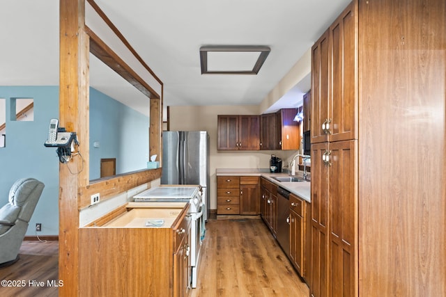 kitchen featuring brown cabinetry, appliances with stainless steel finishes, a sink, light countertops, and light wood-style floors
