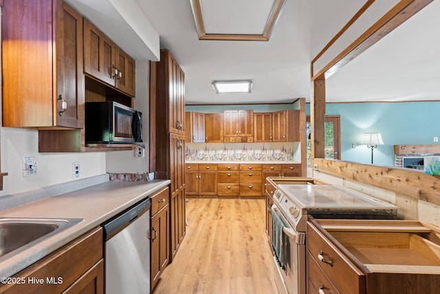 kitchen with light countertops, appliances with stainless steel finishes, brown cabinetry, and light wood-style floors