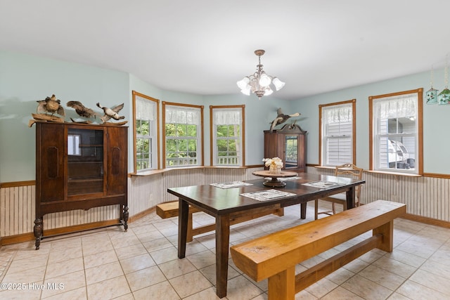 dining space with a wainscoted wall, a wealth of natural light, light tile patterned flooring, and a notable chandelier