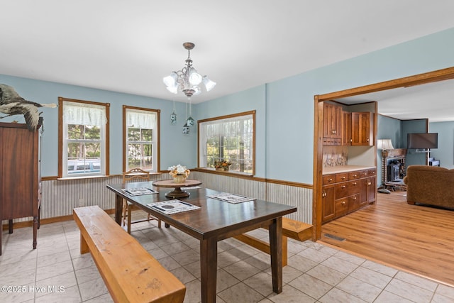 dining space with light tile patterned floors, a chandelier, and a wainscoted wall