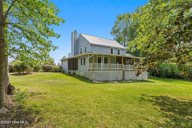 rear view of property featuring a lawn, a chimney, a sunroom, and metal roof