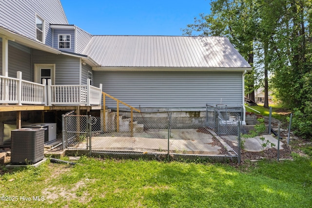 rear view of house with a lawn, central AC, a deck, and metal roof