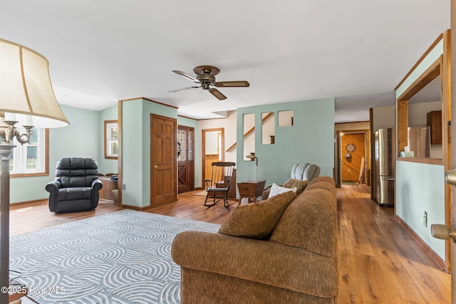 living area with stairs, ceiling fan, baseboards, and wood finished floors