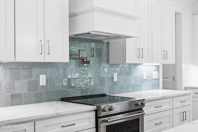 kitchen featuring electric range, tasteful backsplash, light stone counters, white cabinets, and custom range hood