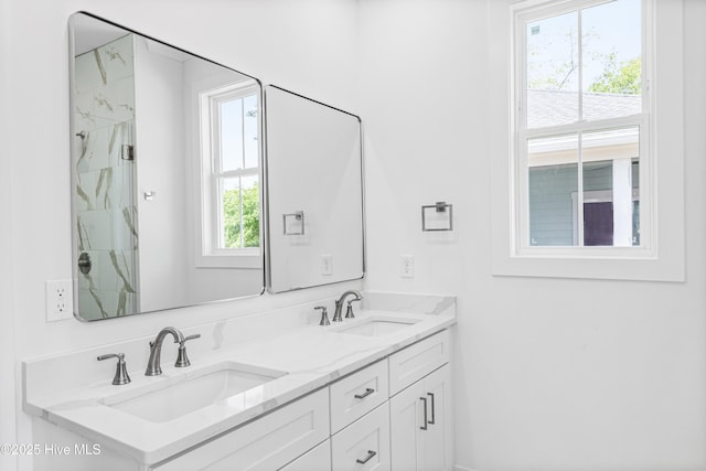 bathroom with double vanity, a marble finish shower, and a sink