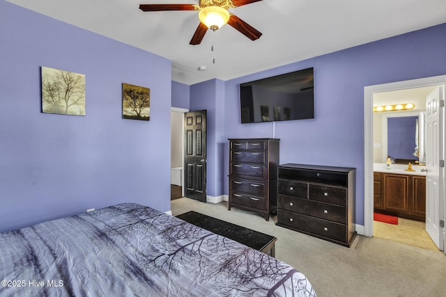 bedroom featuring ceiling fan, light carpet, baseboards, and ensuite bath