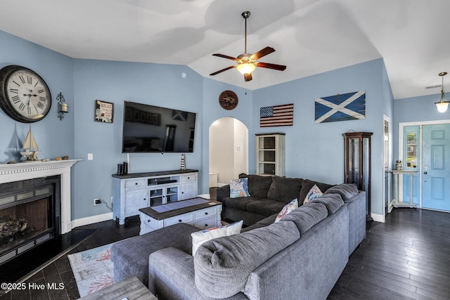 living area with a ceiling fan, a fireplace, baseboards, dark wood-type flooring, and arched walkways