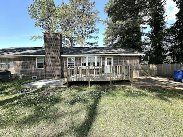 rear view of house with a wooden deck, fence, a chimney, brick siding, and a yard
