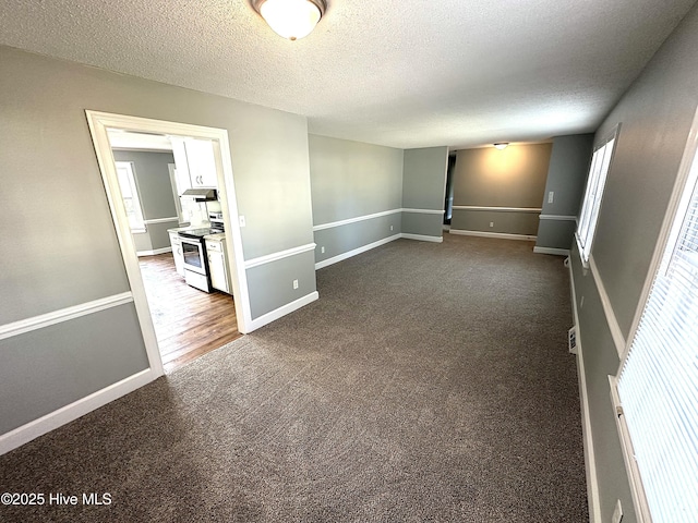 spare room featuring baseboards, a textured ceiling, and dark carpet