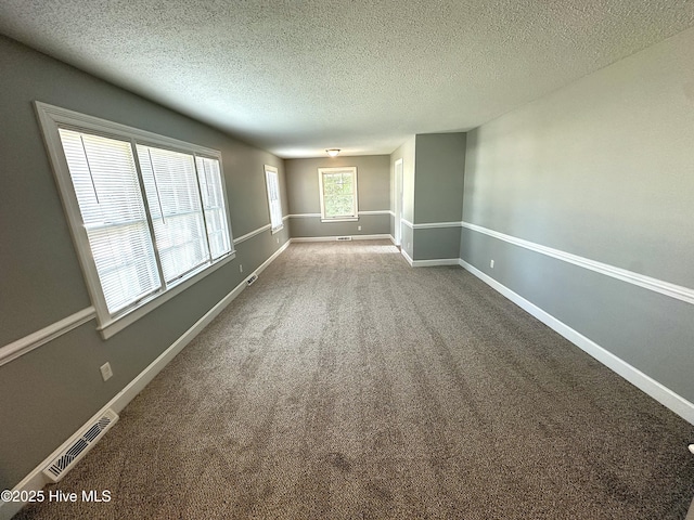 carpeted spare room with a textured ceiling, visible vents, and baseboards