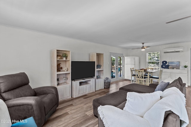 living area featuring ceiling fan, a wall unit AC, french doors, and wood finished floors