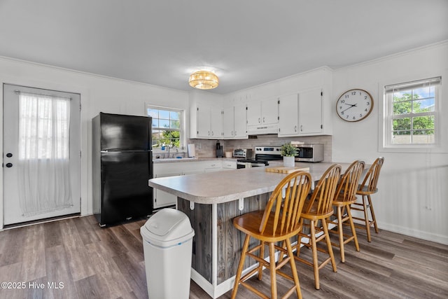 kitchen with appliances with stainless steel finishes, light countertops, a peninsula, a healthy amount of sunlight, and under cabinet range hood