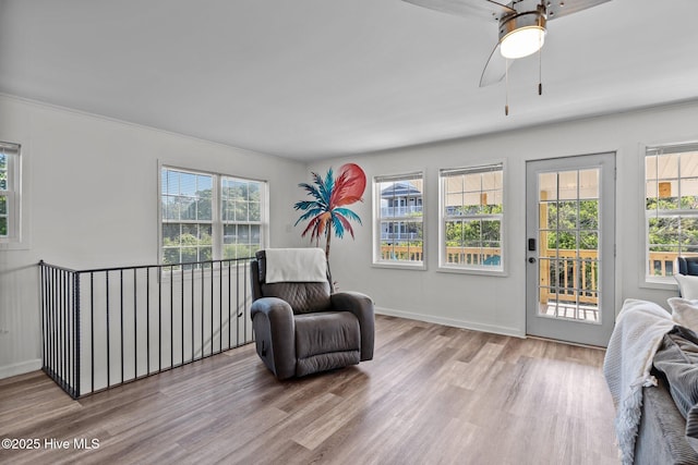 living area featuring crown molding, baseboards, a ceiling fan, and wood finished floors