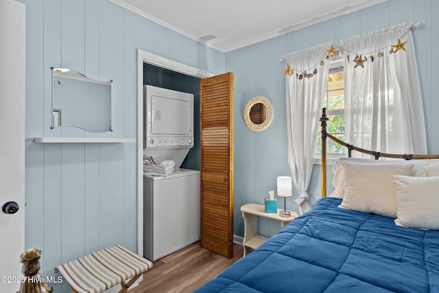 bedroom featuring crown molding, stacked washer / drying machine, and wood finished floors