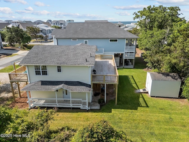 rear view of property featuring an outdoor structure, a wooden deck, roof with shingles, a lawn, and a storage shed