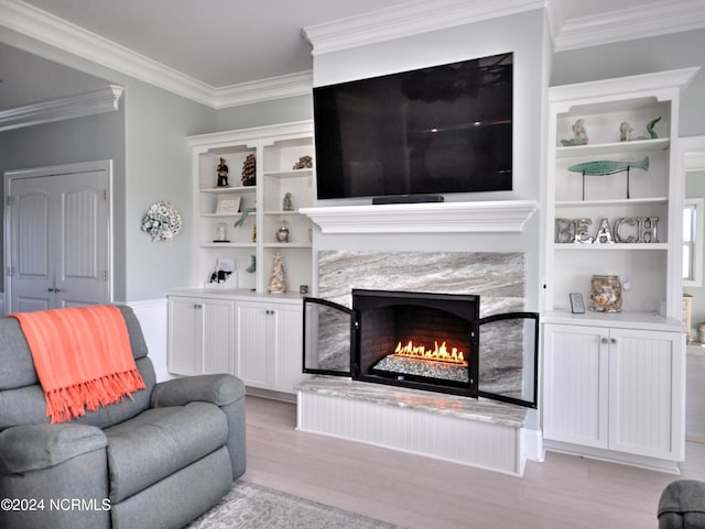 living area with crown molding, a premium fireplace, built in shelves, and light wood-style floors