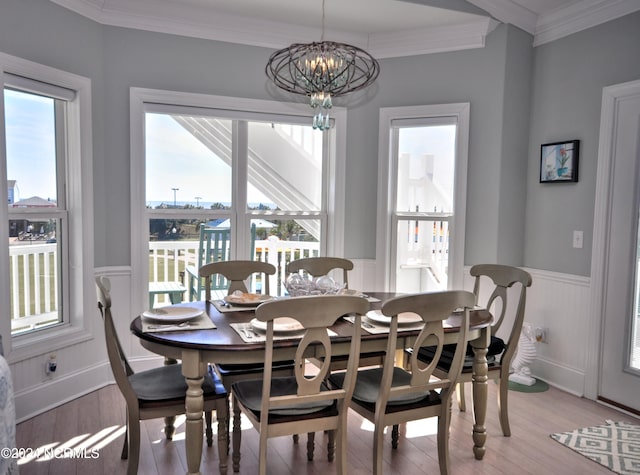 dining room with wainscoting, an inviting chandelier, ornamental molding, and light wood-style floors