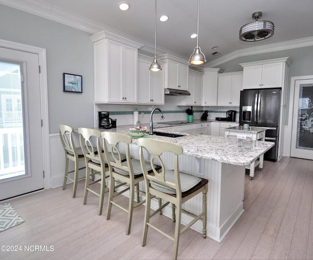 kitchen with ornamental molding, a peninsula, black refrigerator with ice dispenser, under cabinet range hood, and light wood finished floors