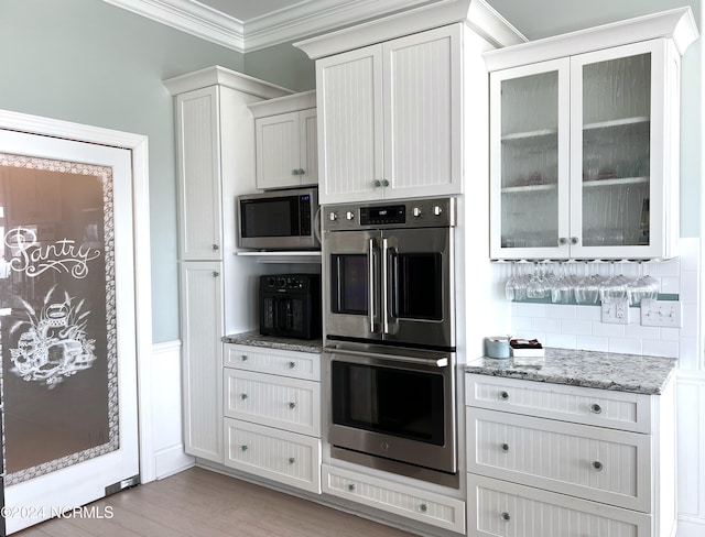 kitchen with ornamental molding, glass insert cabinets, light stone counters, backsplash, and stainless steel appliances