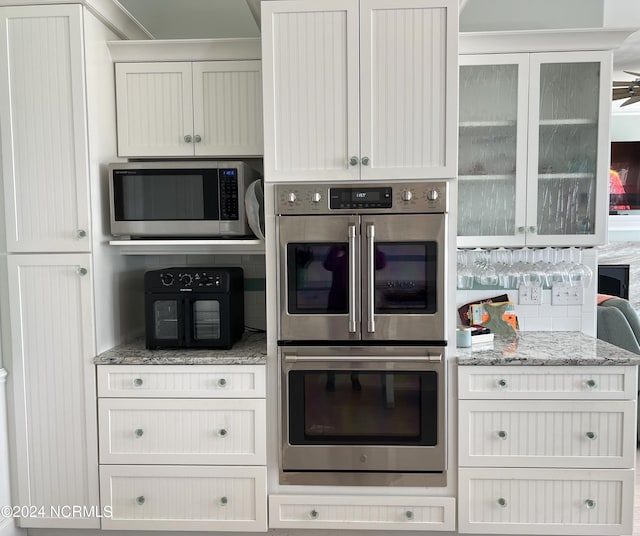 kitchen featuring stainless steel appliances, light stone counters, decorative backsplash, and glass insert cabinets