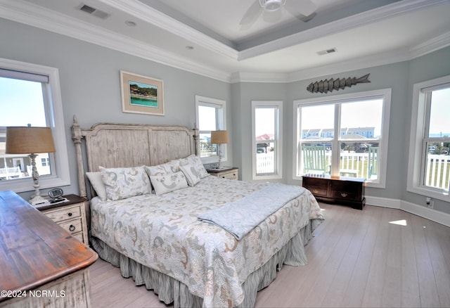 bedroom featuring visible vents, light wood-style floors, crown molding, and a tray ceiling