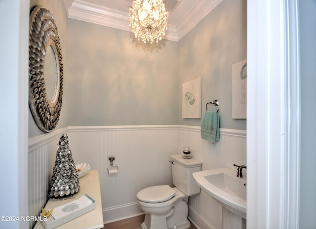 half bathroom featuring crown molding, an inviting chandelier, a sink, toilet, and a wainscoted wall