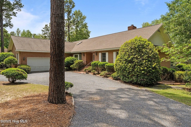 ranch-style house with an attached garage, brick siding, a chimney, a shingled roof, and driveway