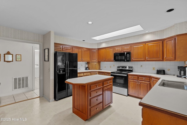 kitchen featuring black appliances, a sink, a skylight, light countertops, and wallpapered walls