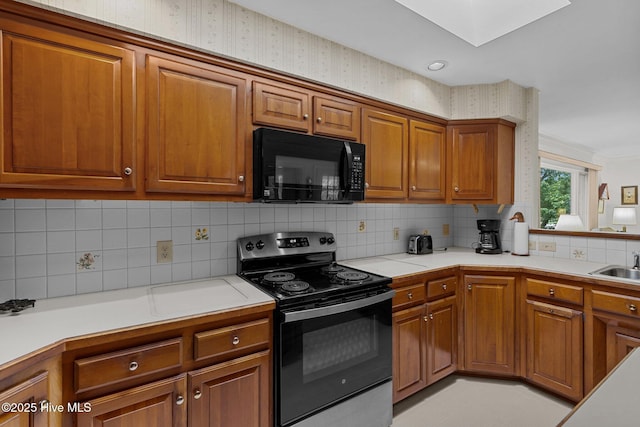 kitchen featuring black microwave, stainless steel electric range, brown cabinetry, a skylight, and light countertops