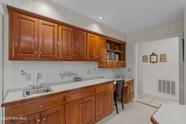kitchen with wallpapered walls, light countertops, a sink, and brown cabinets