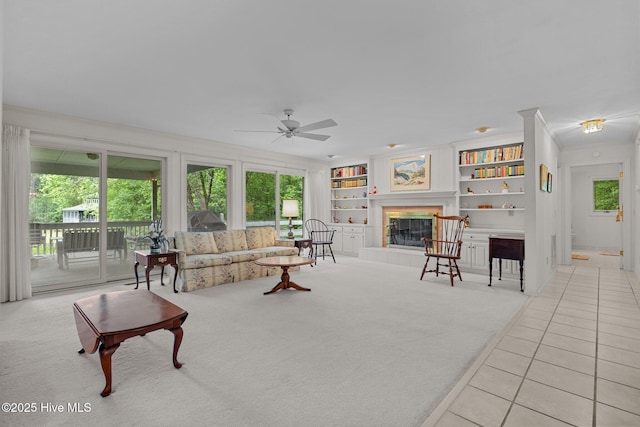 living room with light tile patterned floors, a ceiling fan, ornamental molding, built in shelves, and a tile fireplace