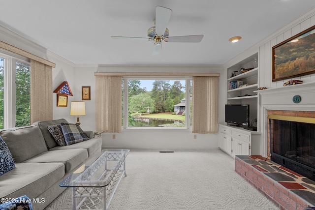 carpeted living area with a ceiling fan, a brick fireplace, baseboards, built in shelves, and crown molding