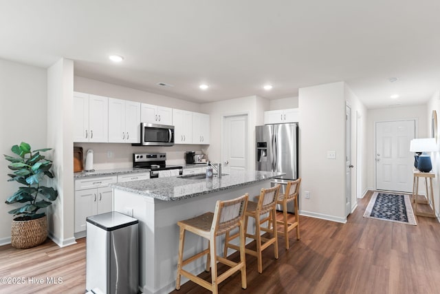 kitchen featuring white cabinets, appliances with stainless steel finishes, a breakfast bar, a sink, and wood finished floors